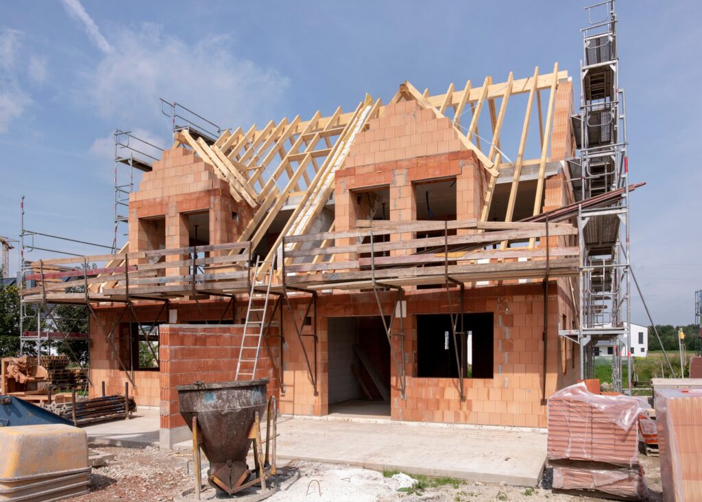 Rohbau eines Doppelhauses mit Dachstuhl und Gerüst | Baustellenzaun